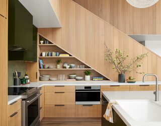 Adding storage under the new stair maximizes the kitchen's footprint. Hemlock wood on the stair was stained to complement the casework. The faucet is from Brizo and the green backsplash tile is Heath.