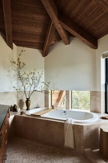 In the angular primary bathroom, “there’s a lot of levels, there’s a lot going on,” says Carine. “ Plaster felt like a really natural element that went with the architectural style of the house, but then it also sort of neutralised the busyness of all the things that were going on.” Travertine parquet tiles line the floor. 