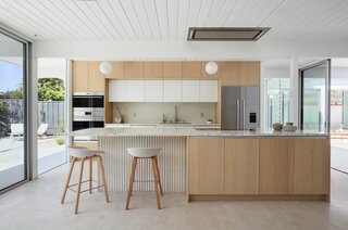 The expanded kitchen has a large central island, with room for prep, seating, storage, and cooking. The cabinetry is a mix of wood, Shinnoki Milk Oak, and white fronts, Fenix NTM Bianco Kos. The terrazzo counters are by Concrete Collaborative. There are two types of tiles: the Mutina Rombini fluted tile on the island and Cepac Krave Sugar Tiles on the backsplash. “It looks very mid-century modern,” says Blaine of the backsplash tile. “But in this application, it also adds that little touch of depth that I think is really important to making the house feel interesting.” The counter stools are from Hay.