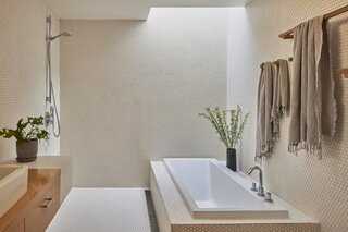 Hexagonal penny tile ascends from floor to ceiling in the skylit primary bathroom.