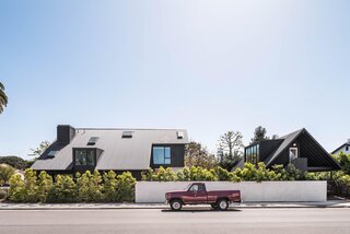 The two structures' gabled roofs can be prominently seen from the street, alongside its all-over black siding.